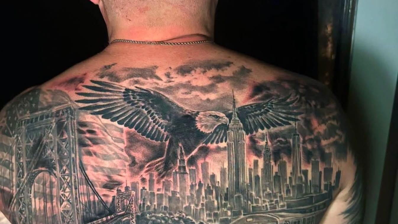 A large black and grey back piece of an eagle over a city skyline, covering the shoulders and spine.