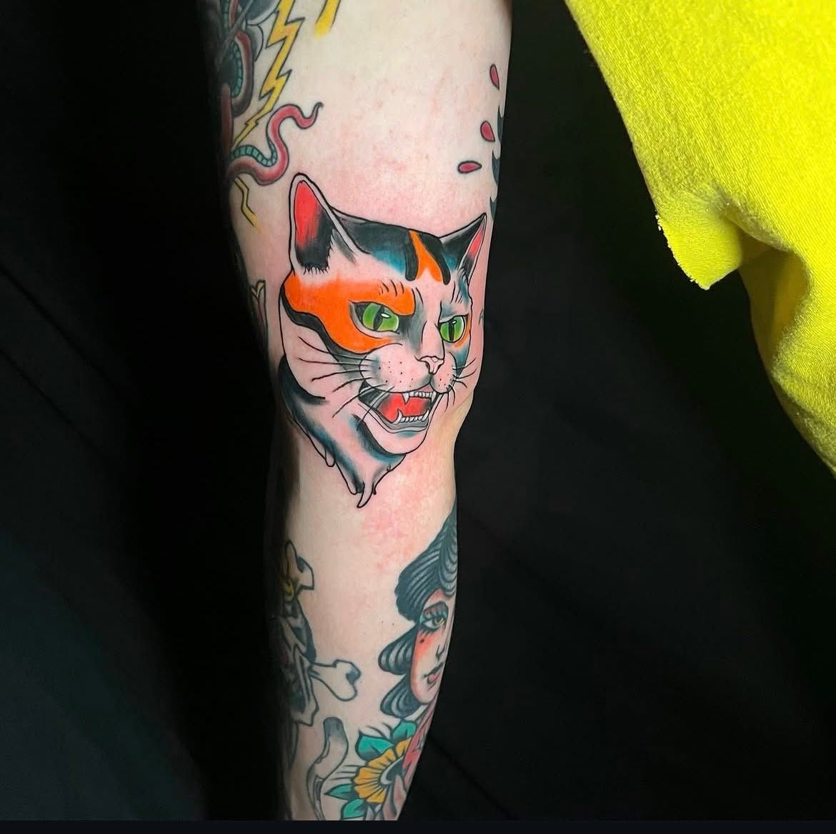 Colour portrait of a calico cat tattooed on a forearm.