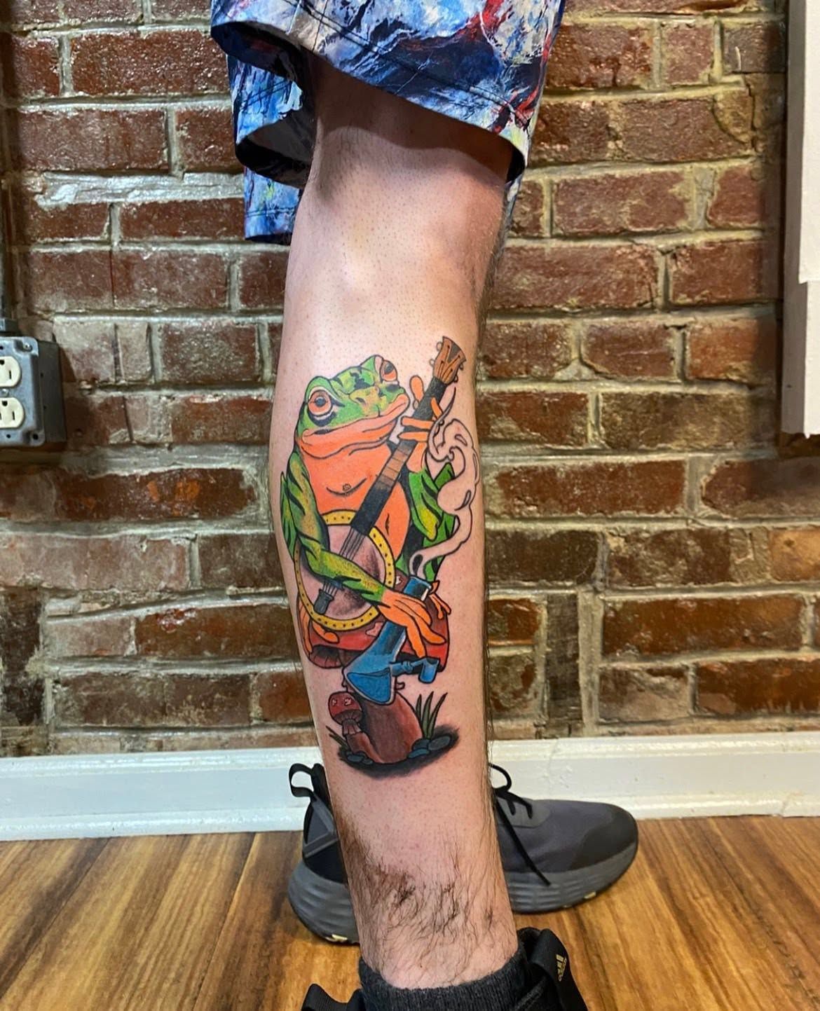 Full colour character tattoo on a lower leg, photographed against brick.