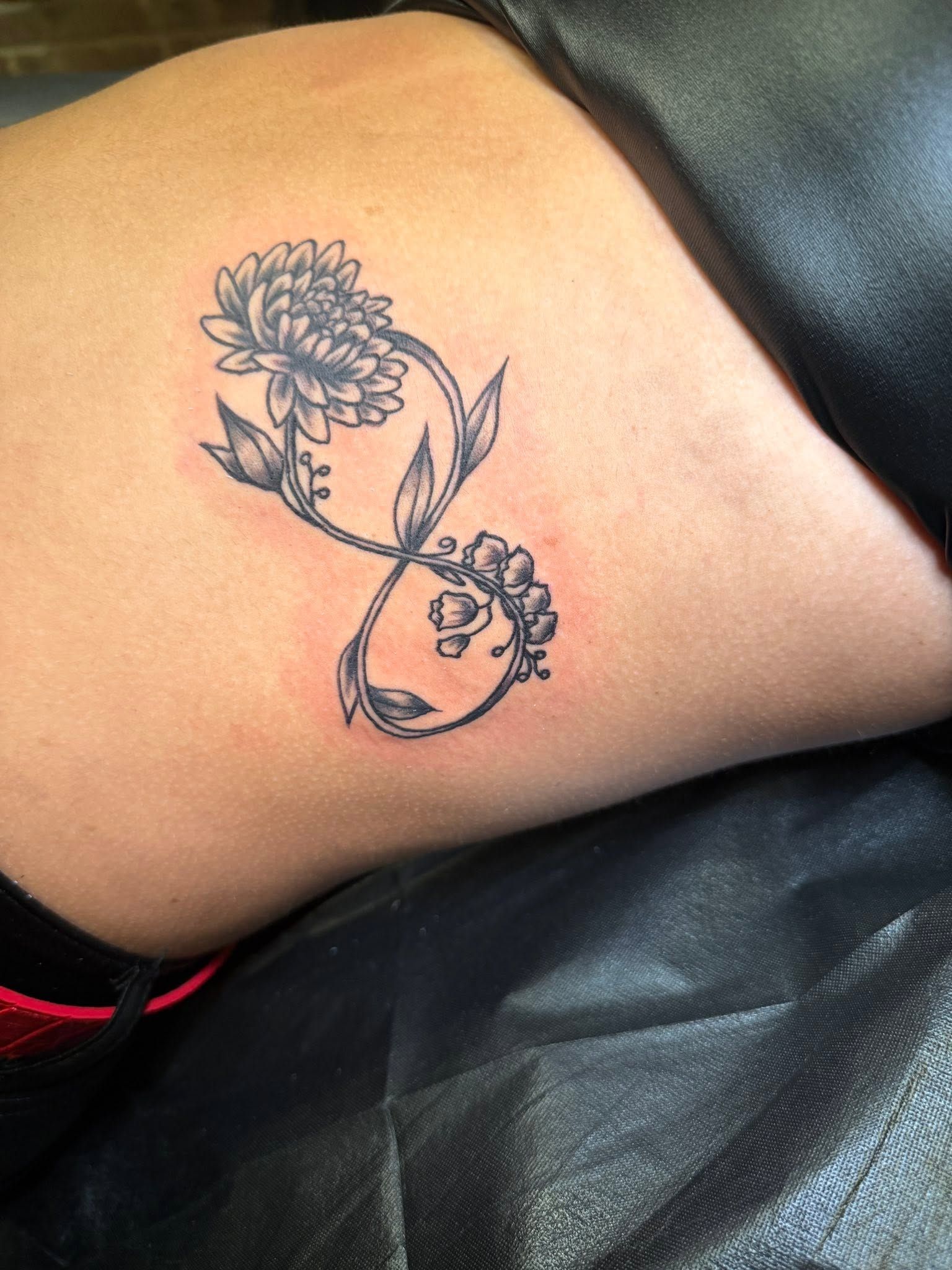 Fine line floral and infinity design tattooed on a shoulder blade.
